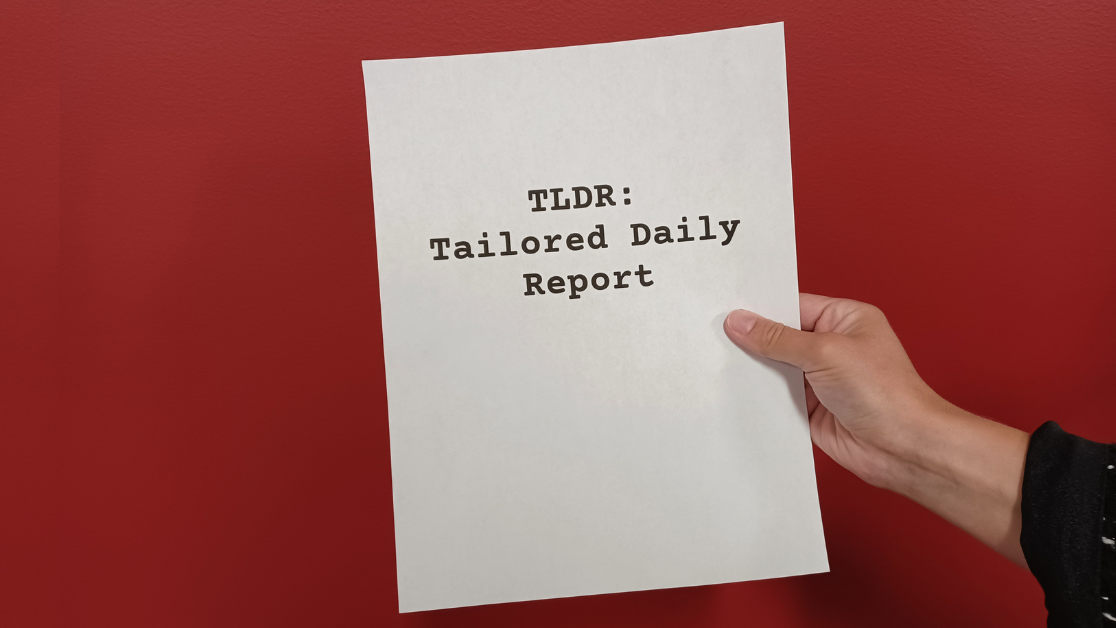 Hand holding up a sheet of paper that says “TLDR: Tailored Daily Report” in front of a red backdrop.