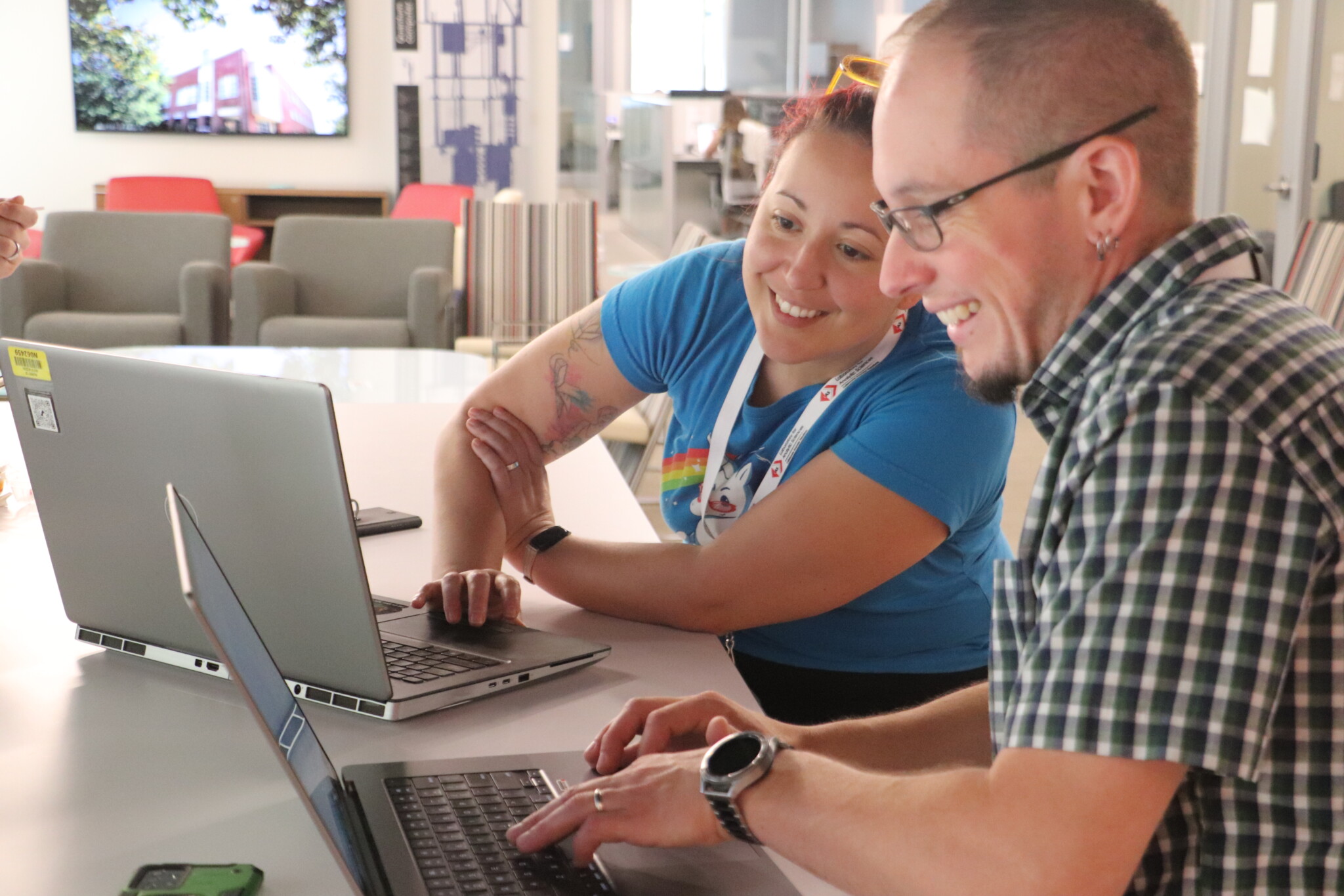 Two people smiling and working together at their laptops.