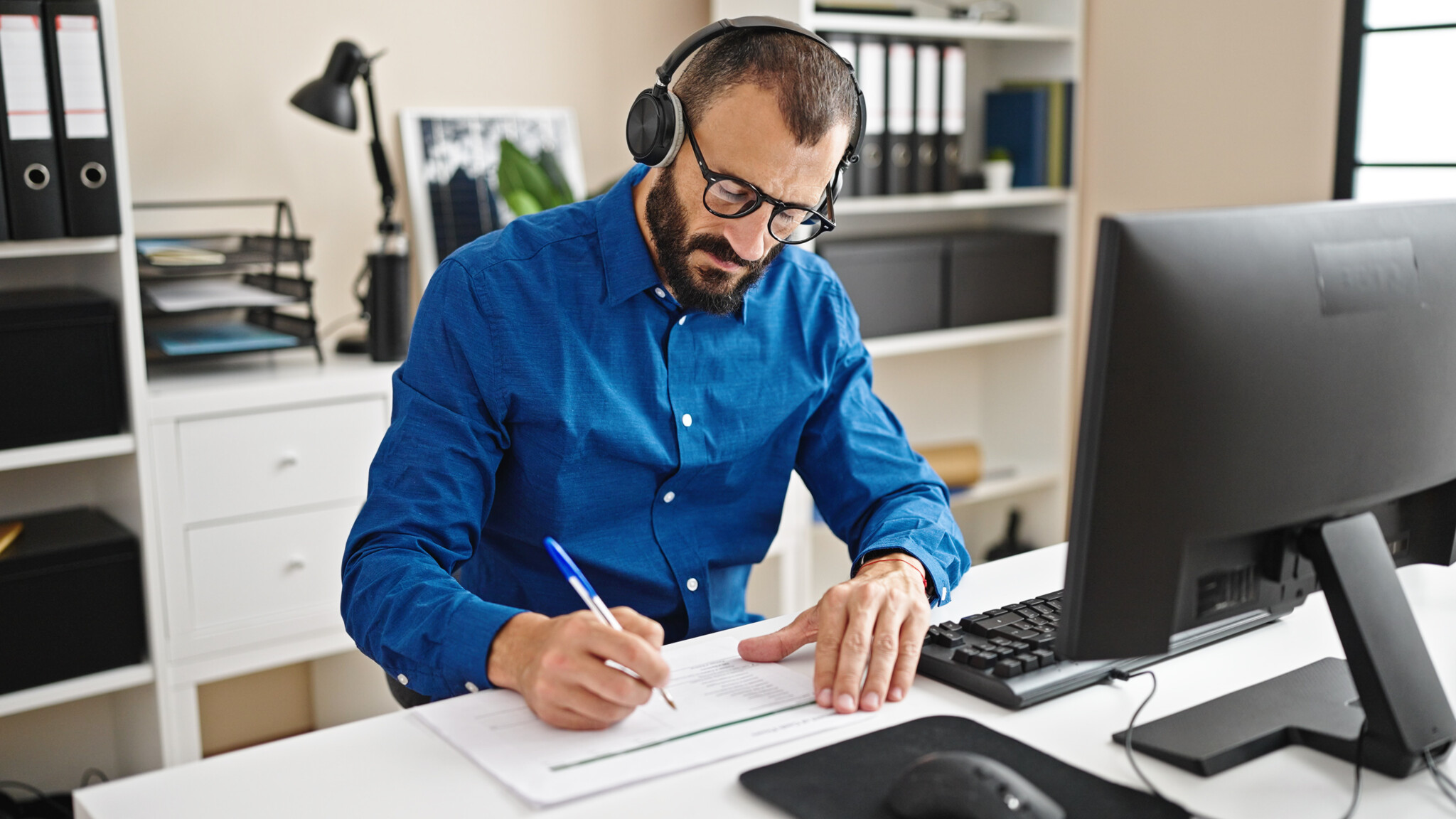 Worker using computer and headphones taking notes at office