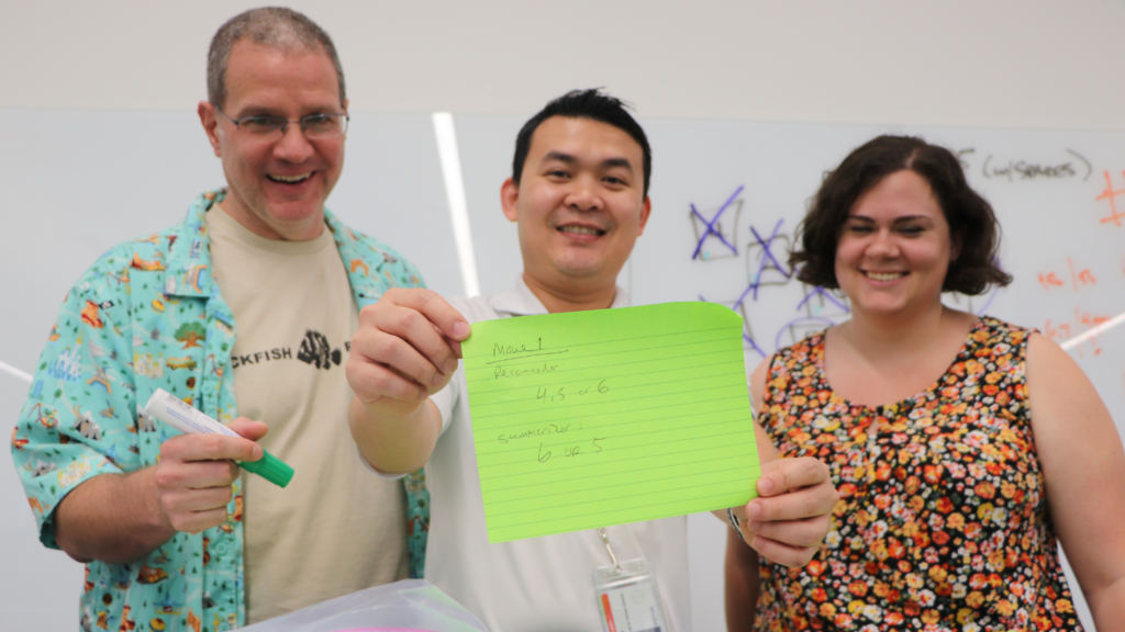 Three people holding up a sticky note