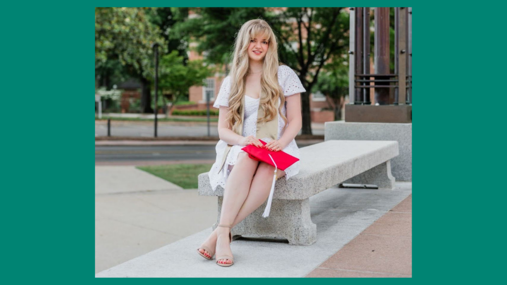 Celia sitting on a marble bench, holding a red graduation cap.