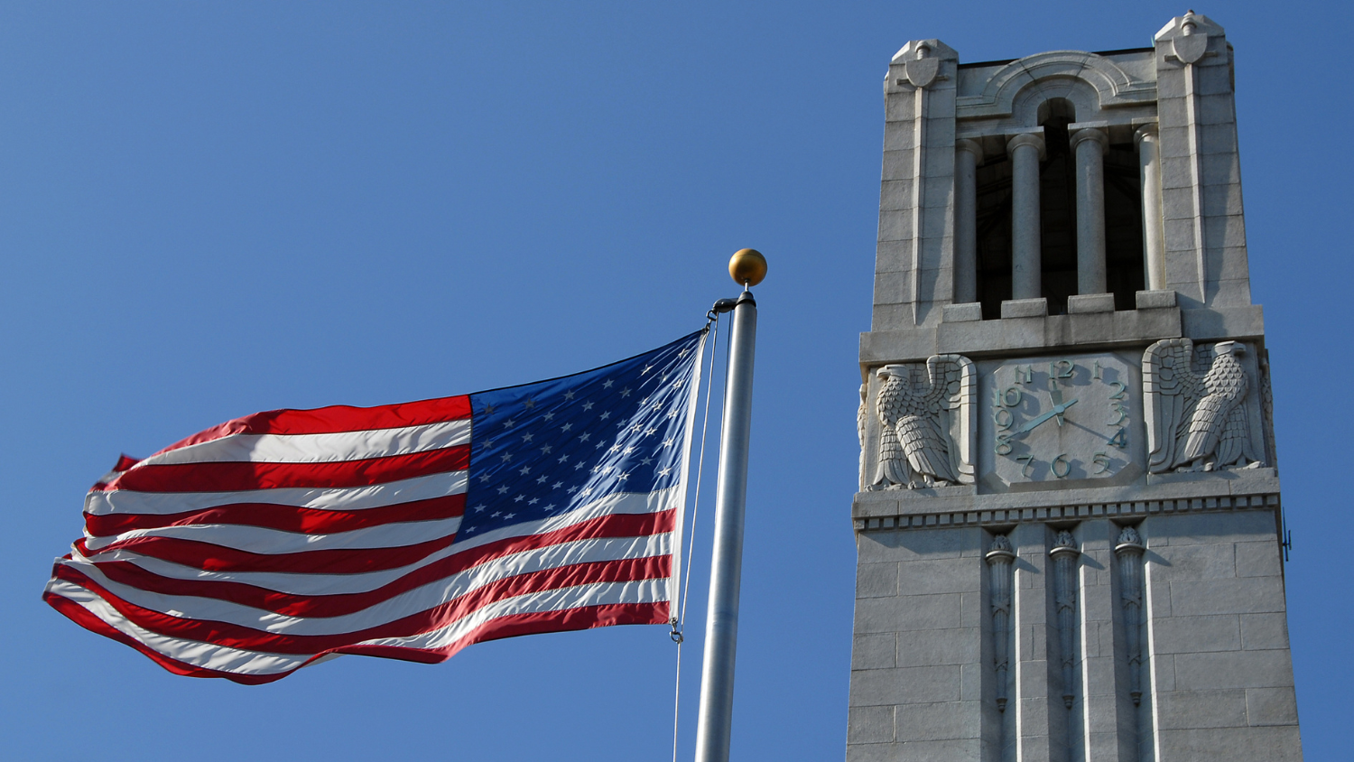 The American flag waves in the breeze beside the NC State Memorial Belltower.