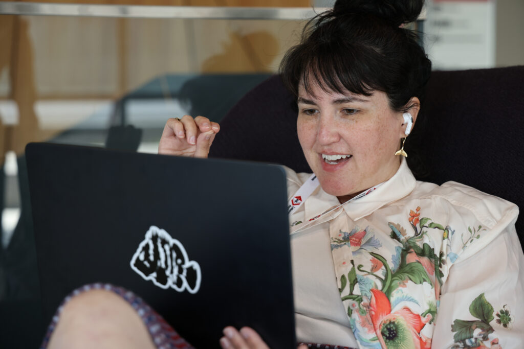 A person speaking on a video call. She is wearing earbuds holding a laptop.