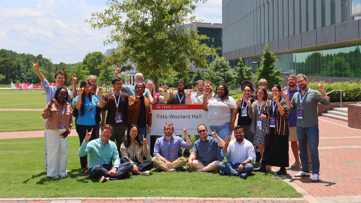 Group of 20 people outside making the "Wolfie" hand sign for NC State pack pride.