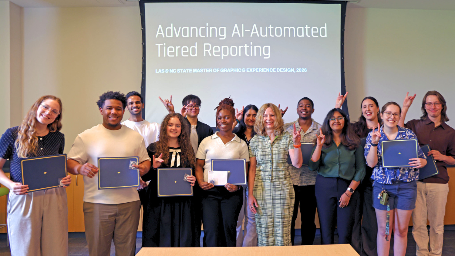 Twelve students and their professor smile and give the "Wolfie" hand sign for NC State.