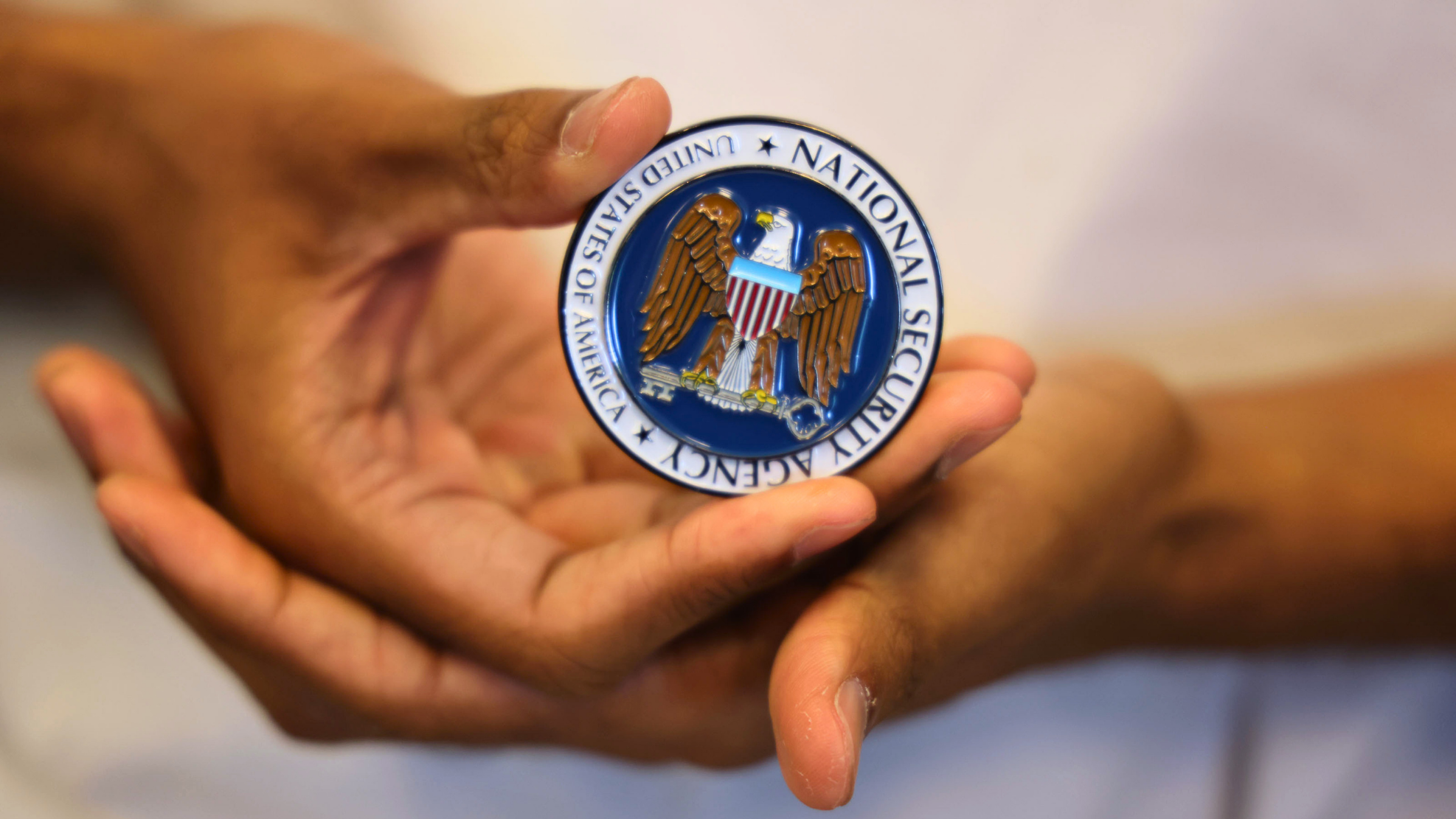 Close up of hands holding an enameled coin featuring the National Security Agency logo.